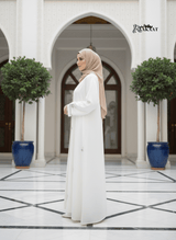 White Embroidered Abaya đ€ A0002 worn by a woman in a stylish setting with plants and elegant architecture.