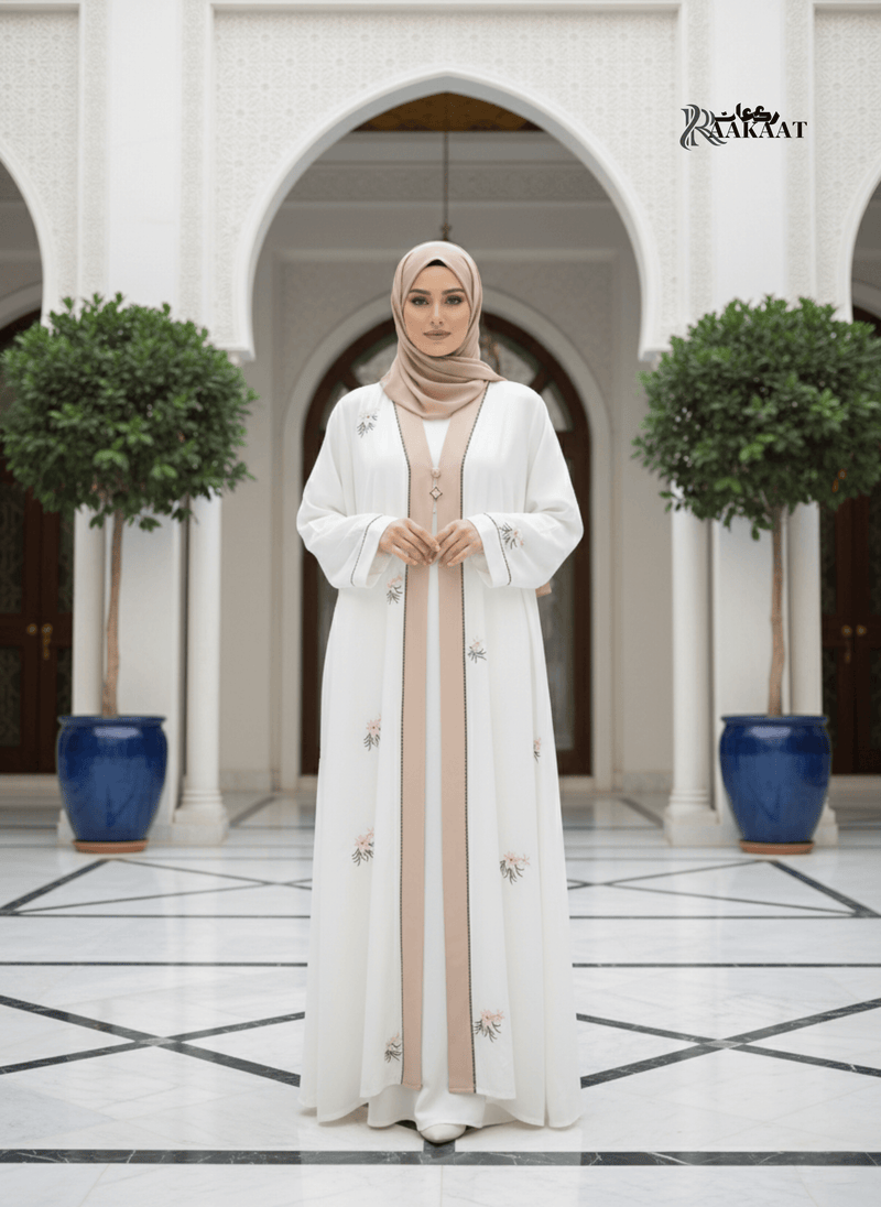 White Embroidered Abaya 🤍 A0002 worn by a woman in an elegant setting with floral embroidery and a neutral hijab.