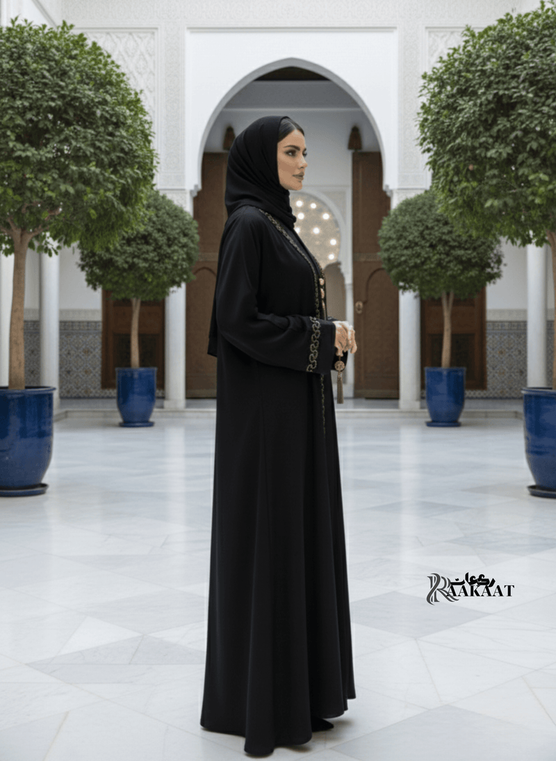 🖤 Classic Black Abaya with Gold Embroidery – Timeless Luxury 🖤 A0003 worn by a model in a luxurious courtyard.