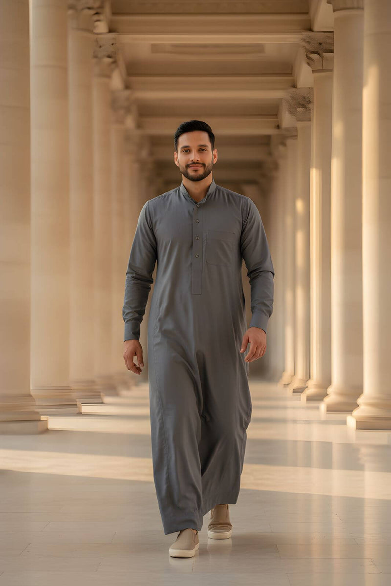A man wearing The Obsidian Slate Contemporary Thobe, walking elegantly in a stylish setting, showcasing modern tailoring.
