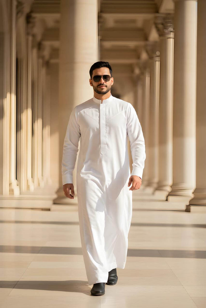 The Pristine White Thobe: Saudi Heritage & Modern Minimalist T0001 worn by a stylish man in a sunny corridor.