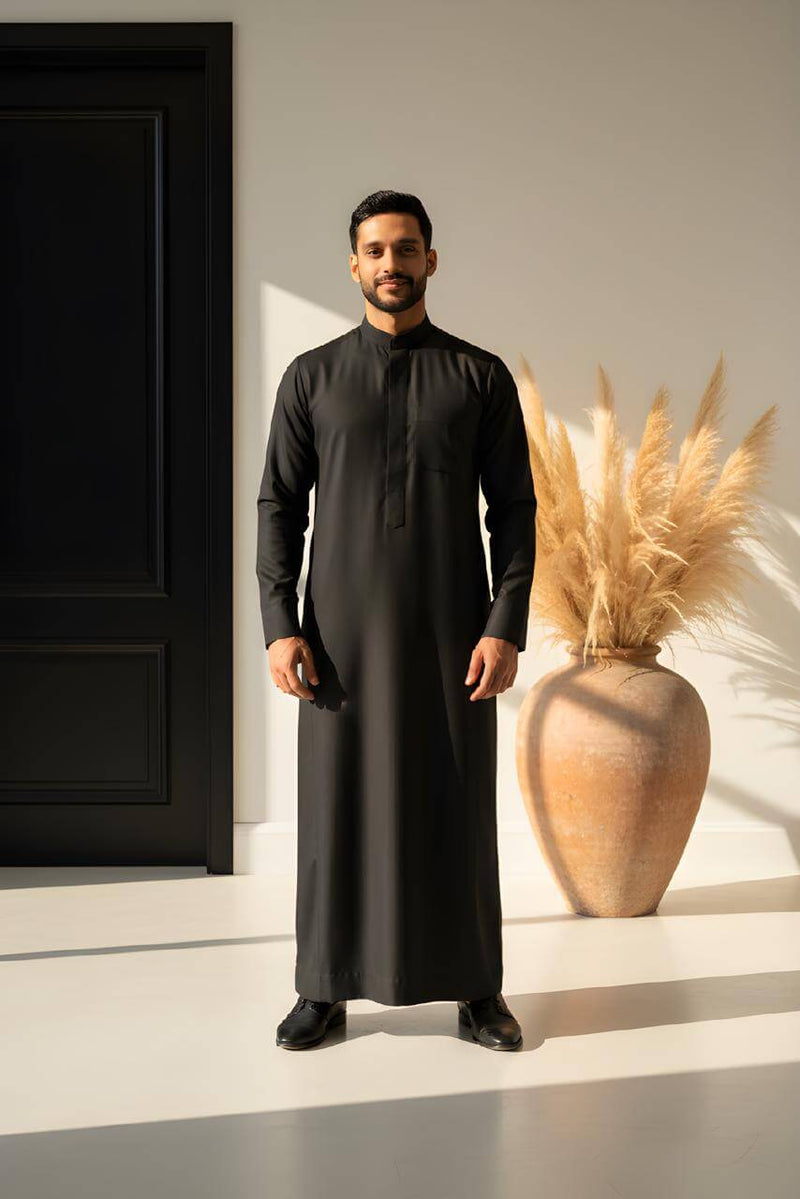 The Obsidian Executive Saudi Thobe worn by a man in a stylish setting with a modern decor.