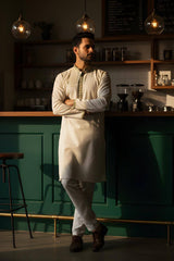 A man in an elegant ivory The Alabaster Heritage Panjabi P0009, standing in a stylish café.
