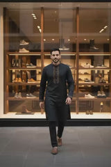 Classic Black Bangladeshi Panjabi with Elegant Golden Embroidery P0002 worn by a man walking in a stylish shoe store.
