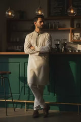 A stylish man wearing The Alabaster Heritage Panjabi P0009, standing relaxed at a café bar, showcasing elegance.
